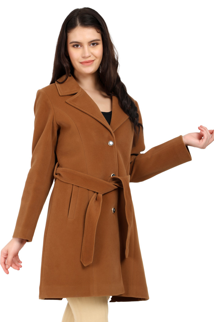 A standing pose of a woman in black shades, wearing Trufit’s Long Dk. Camel Velvet coat with a lapel collar, button closure, belt, side pockets, and skin bell bottom, holding a clutch from her left hand and her right hand in the pocket.